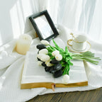 Open book with black and white tulips, a cup, and a candle on a white surface.