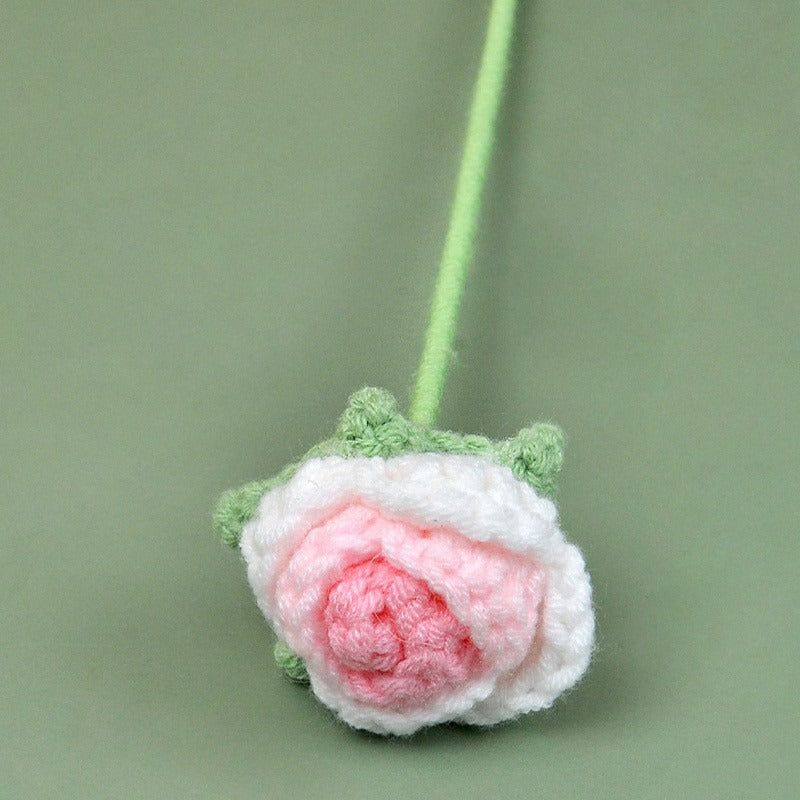 Crocheted flower with pink center and green leaves on a light green background