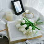 Open book with white tulips, a candle, and a cup on a white fabric background