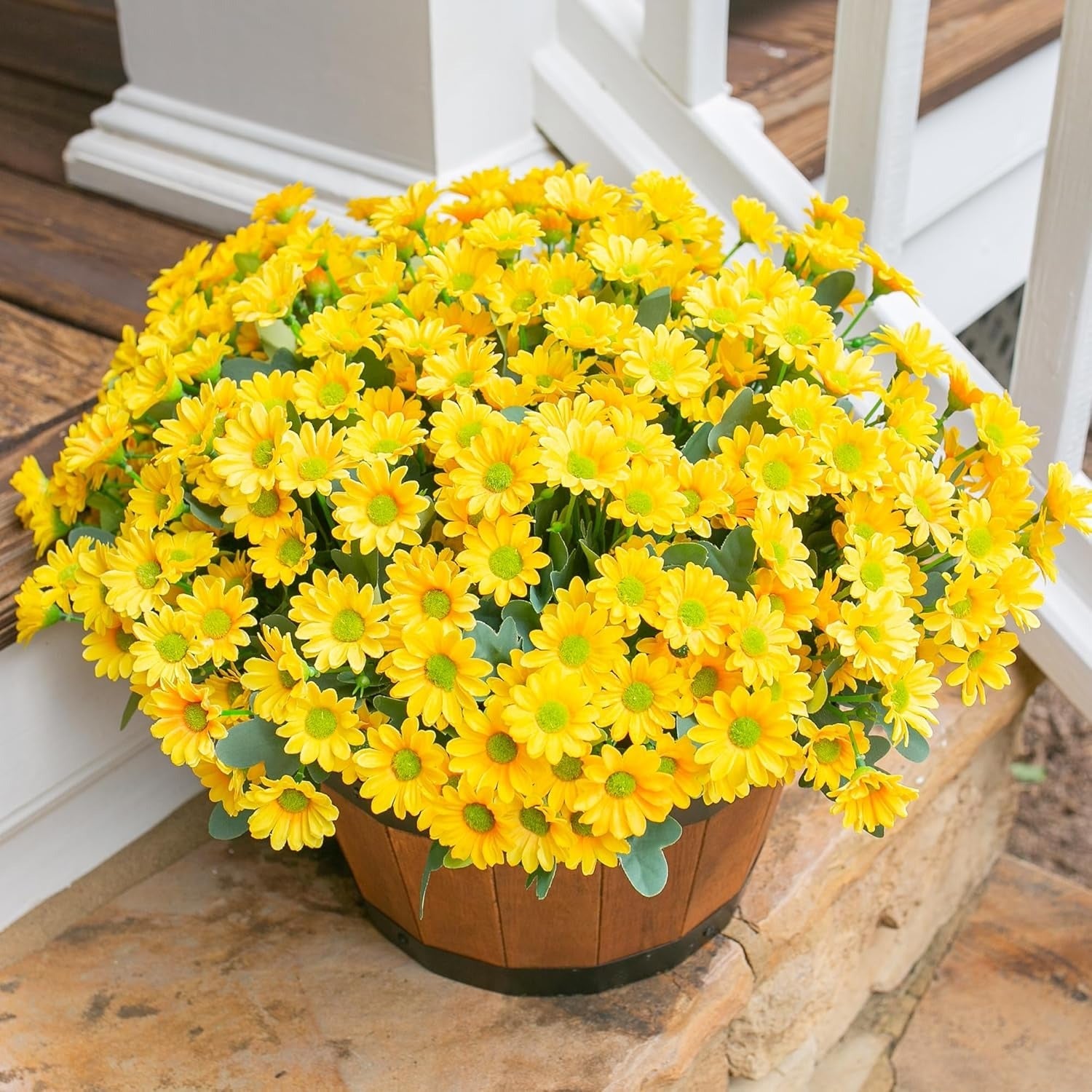Potted yellow flowers on a stone surface with a white chair in the background