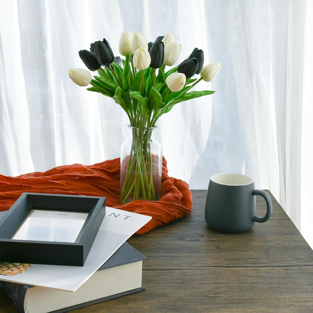 Vase with black and white tulips on a wooden table with a mug and books.