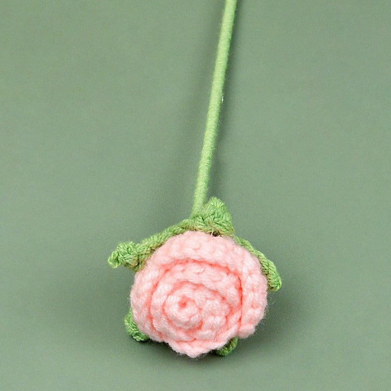 Pink crocheted flower with green stem on a green background