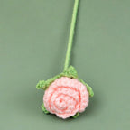 Pink crocheted flower with green stem on a green background