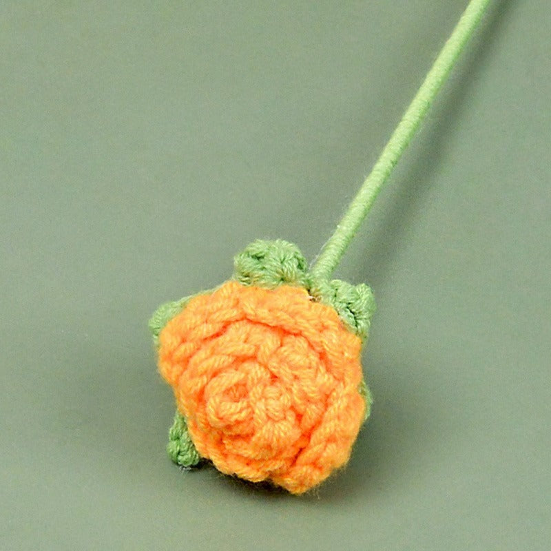 Crocheted orange strawberry with green leaves on a light green background