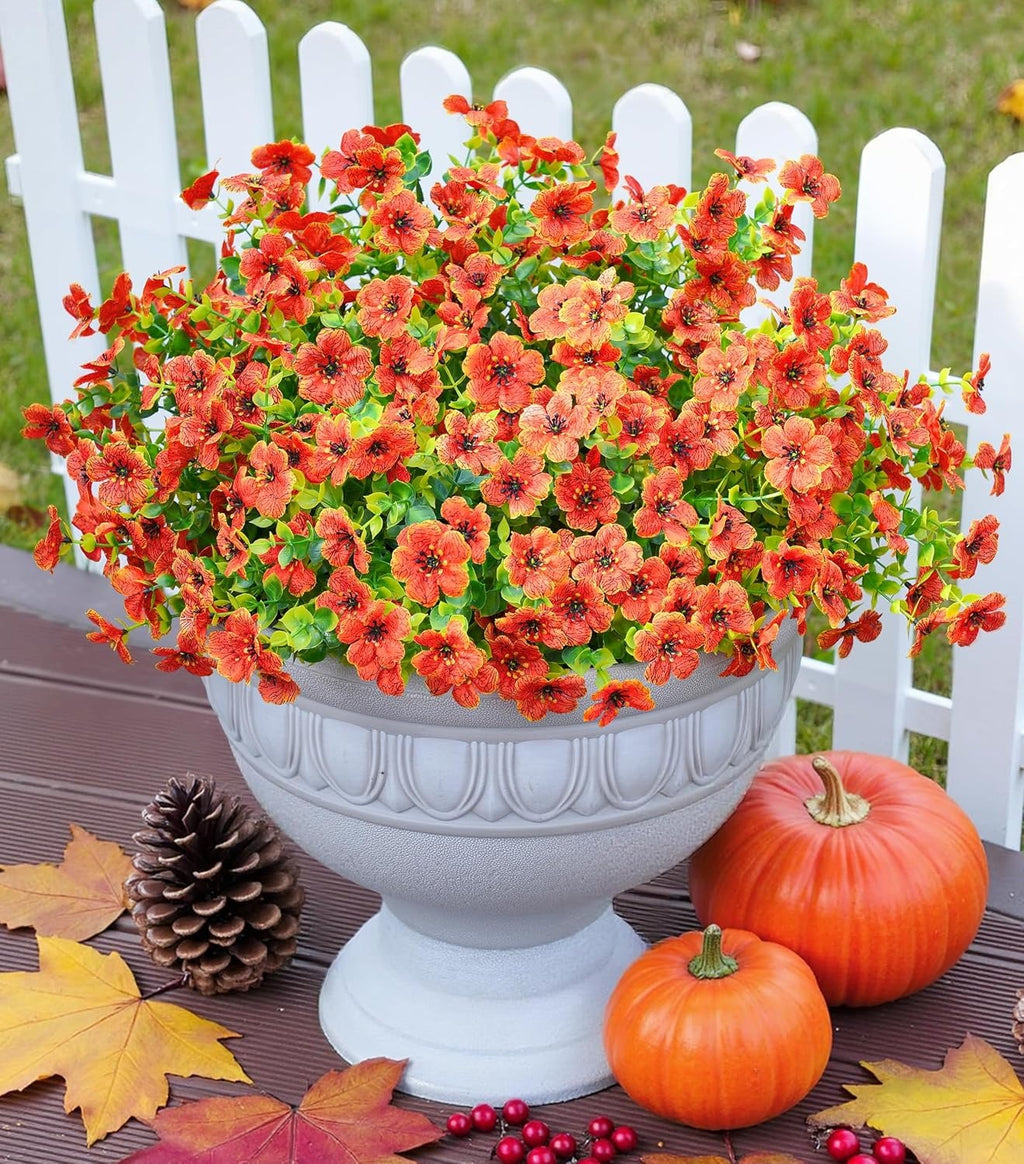 Floral arrangement in a decorative pot with pumpkins and leaves on a wooden surface.
