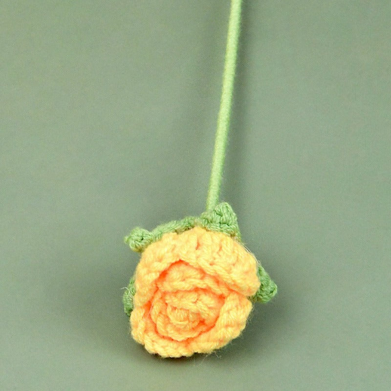 Crocheted orange flower with green stem on a green background