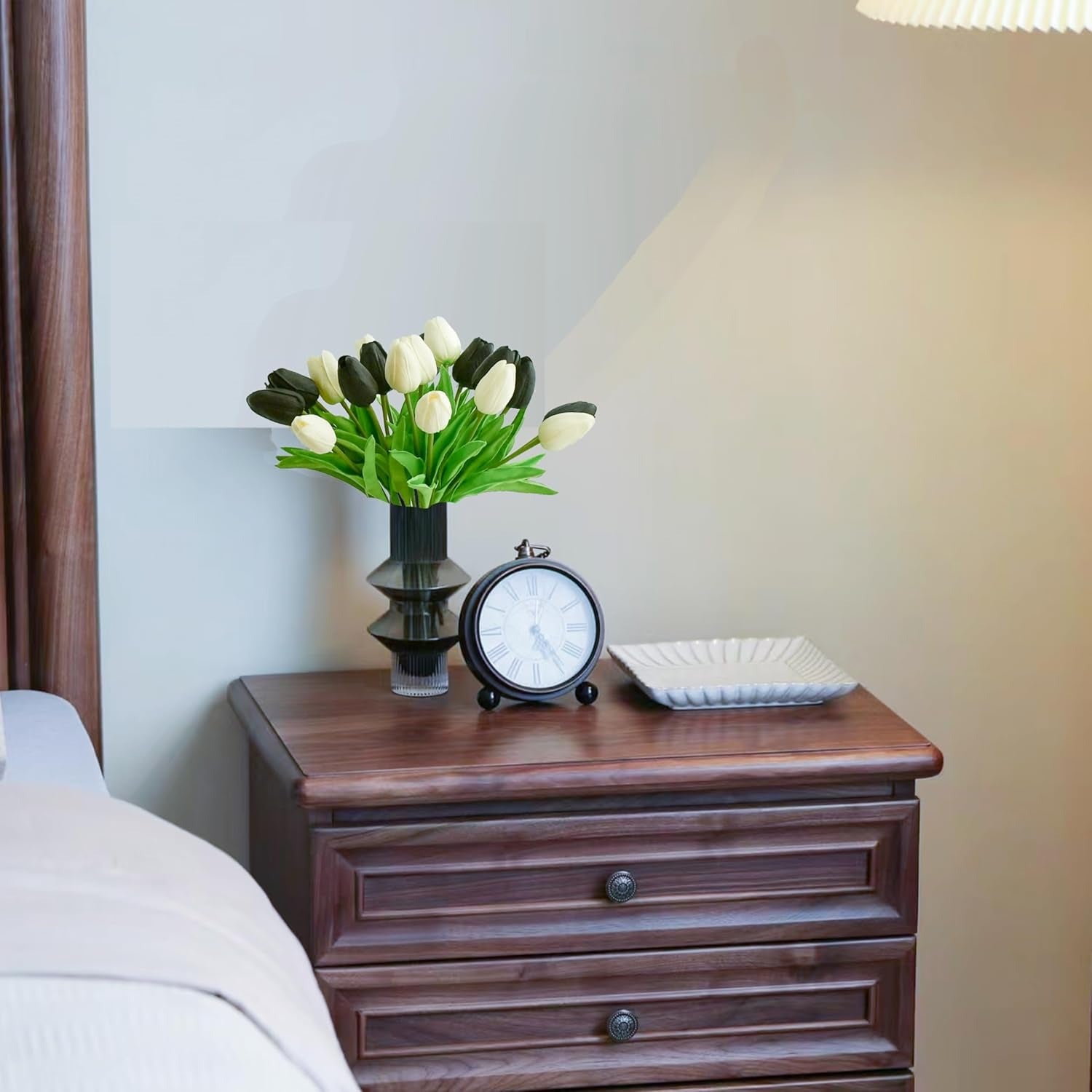 Wooden nightstand with decorative items including a vase of flowers, clock, and square plate.