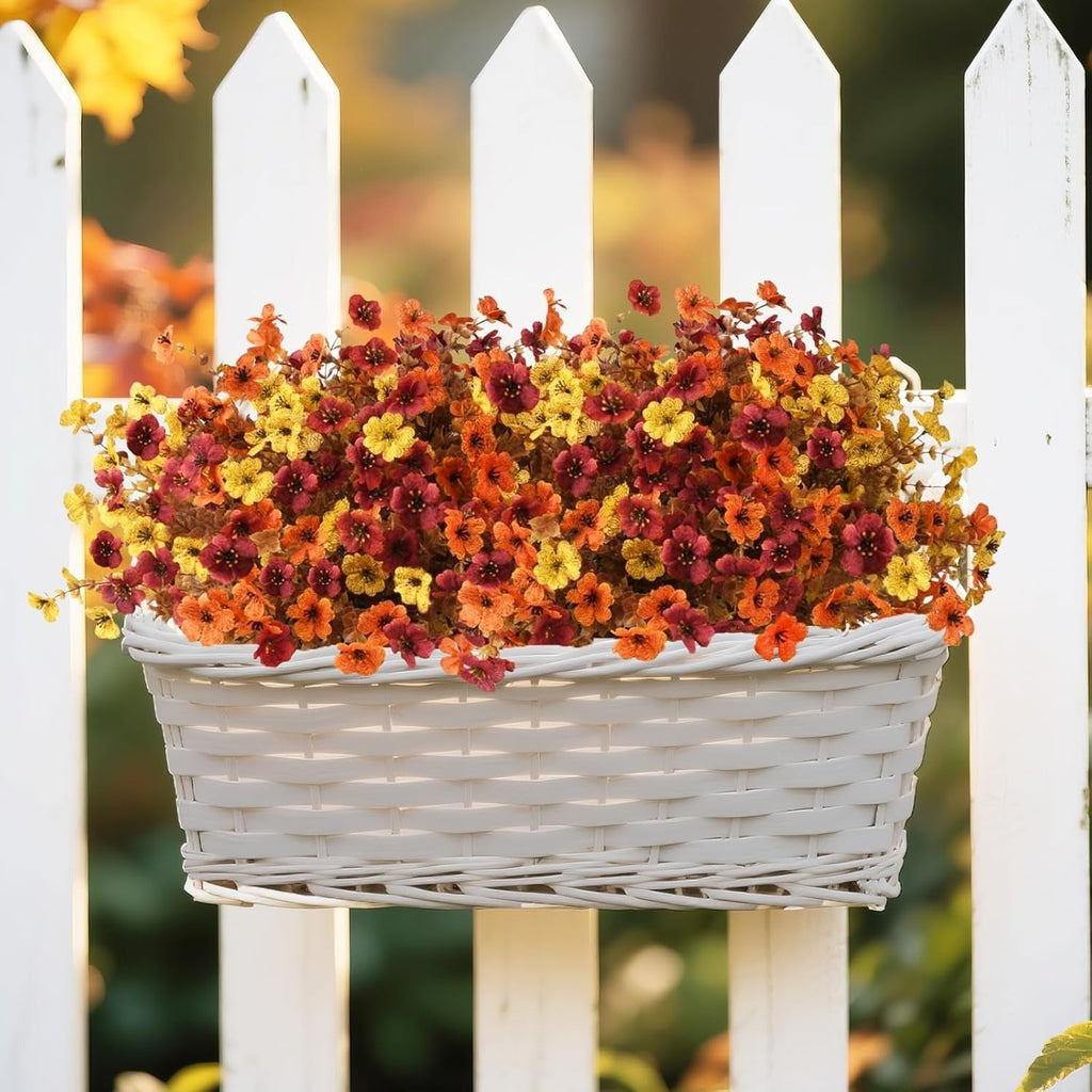 Basket of autumn-colored flowers against a white picket fence