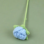 Blue crocheted flower with green stem on a green background