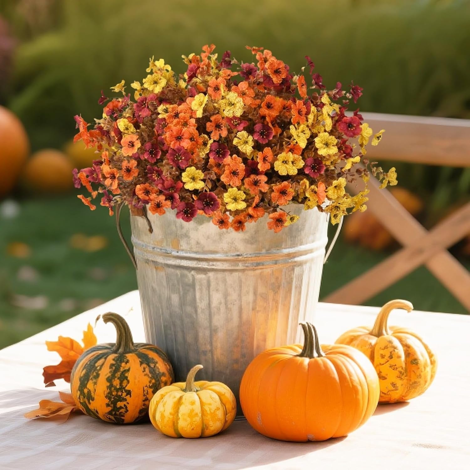 Metal bucket with autumn flowers and pumpkins on a table outdoors