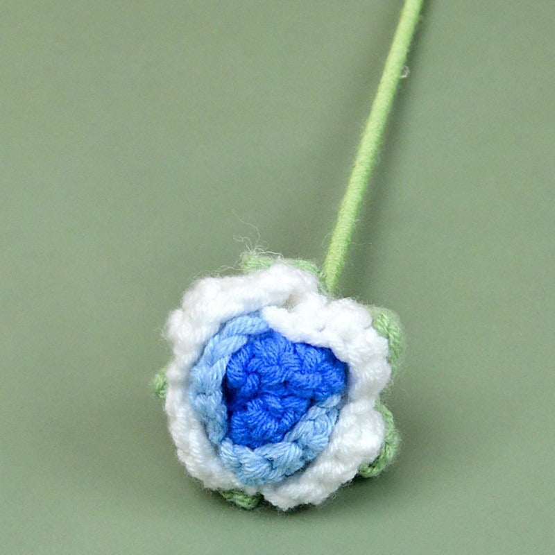 Crocheted flower with blue center and white petals on a green background
