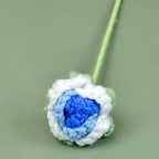 Crocheted flower with blue center and white petals on a green background