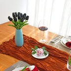 Dining table setting with black tulips in a blue vase, a glass of red wine, and decorative plates.