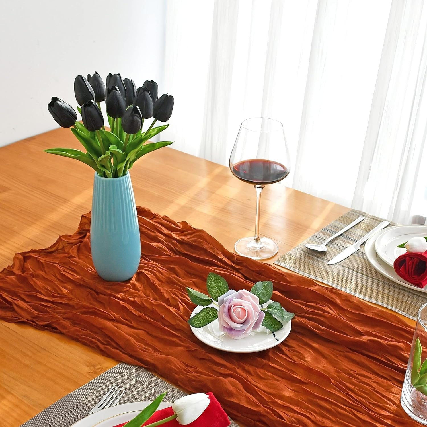 Dining table setting with black tulips in a blue vase, a glass of red wine, and decorative plates.
