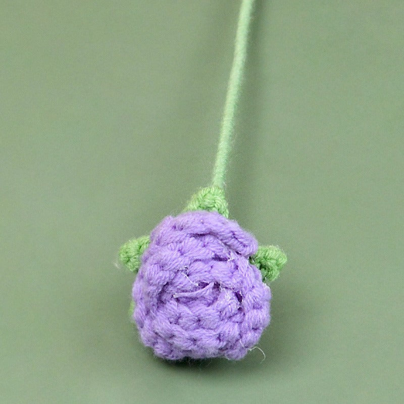 Crocheted purple flower with green stem on a green background
