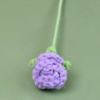 Crocheted purple flower with green stem on a green background