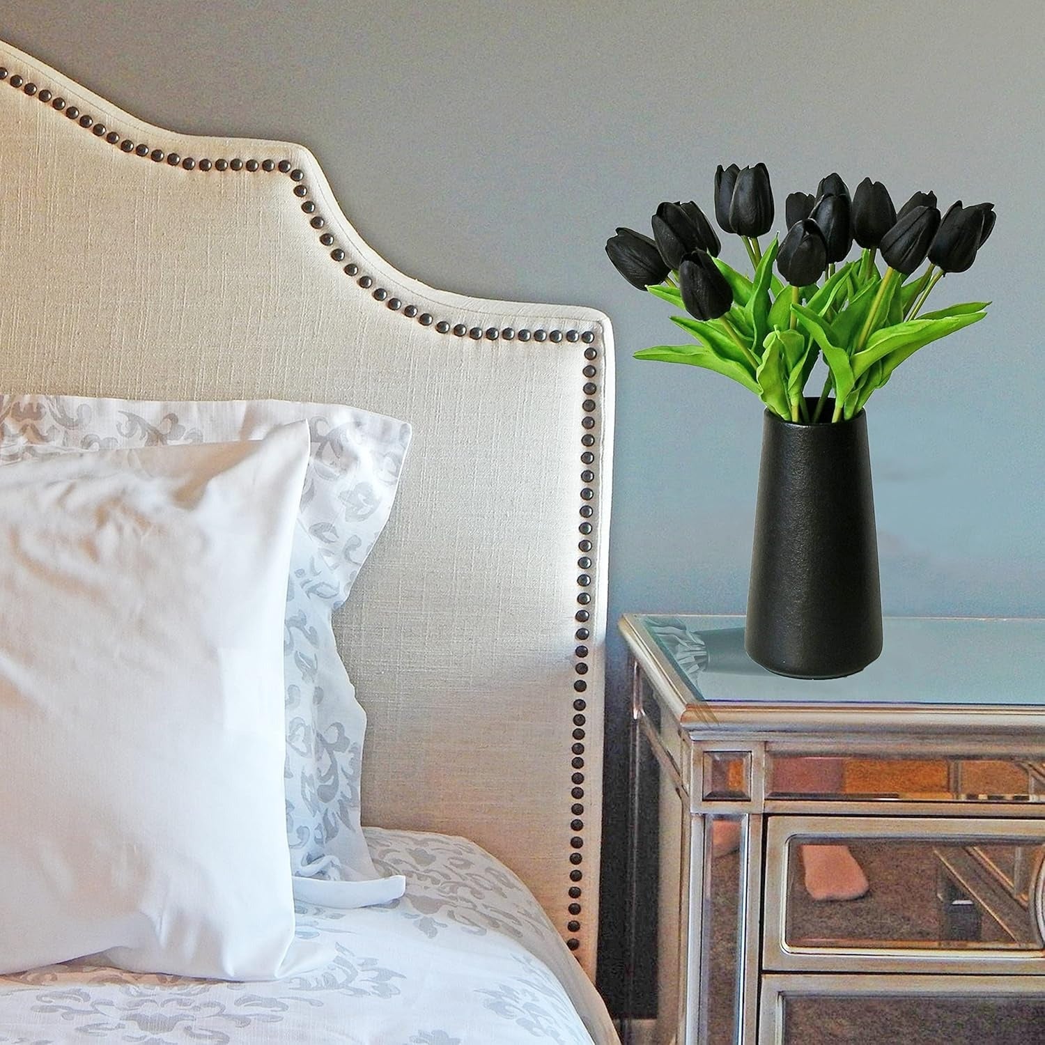 Decorative vase with black tulips on a nightstand next to a bed with white pillows.