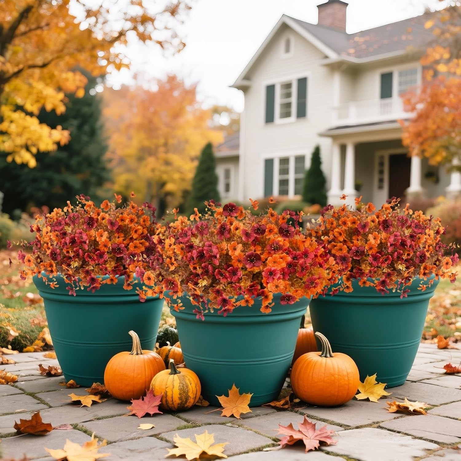Teal pots with autumn-colored flowers and pumpkins on a patio in front of a house.