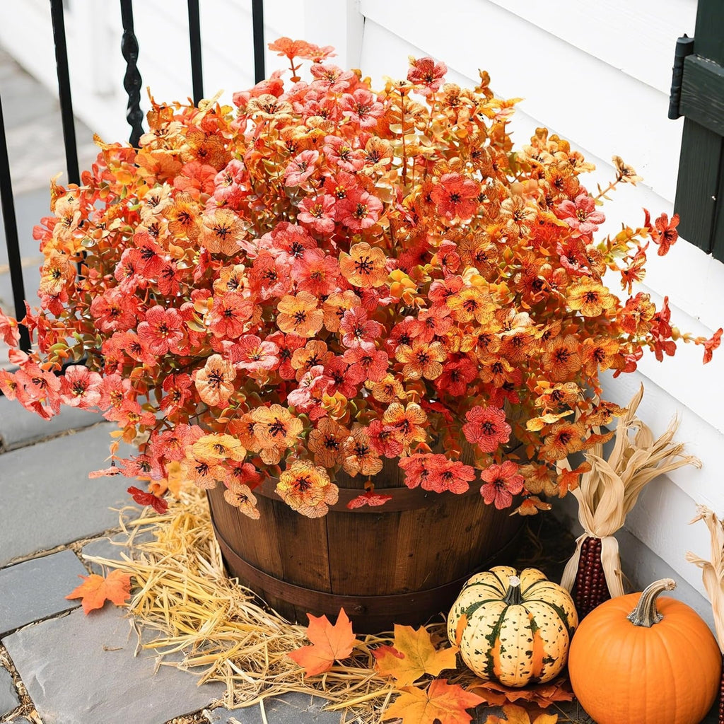 Decorative arrangement with autumn flowers in a wooden barrel, pumpkins, and fall leaves on a porch.