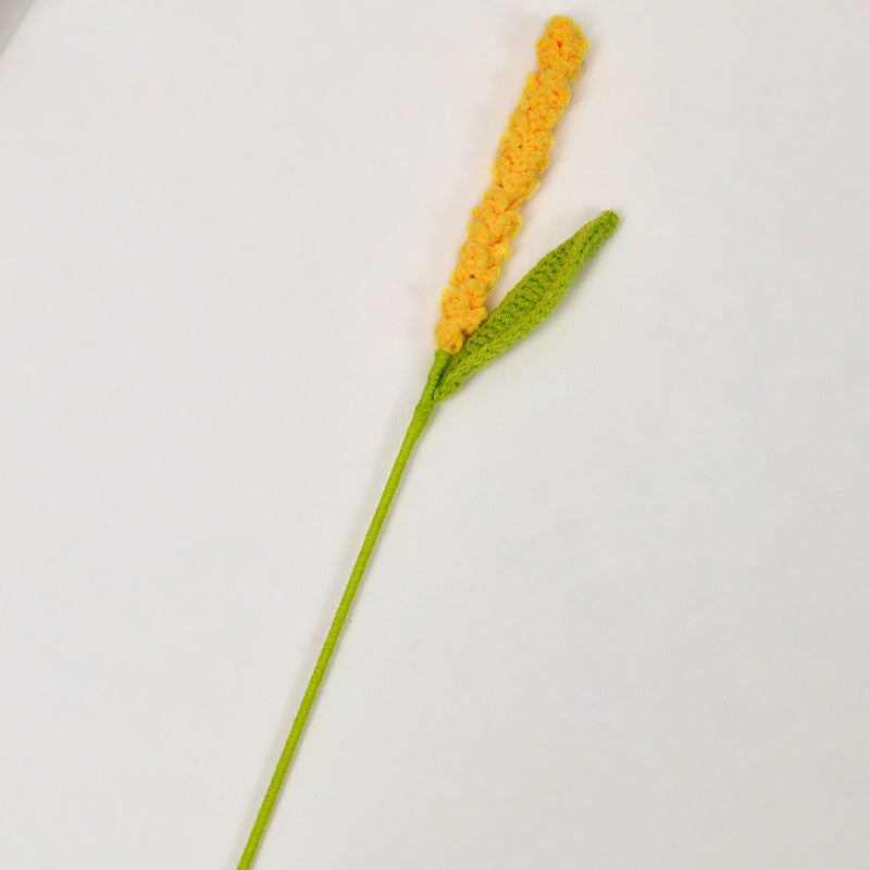 Crocheted yellow flower with green stem on a white background