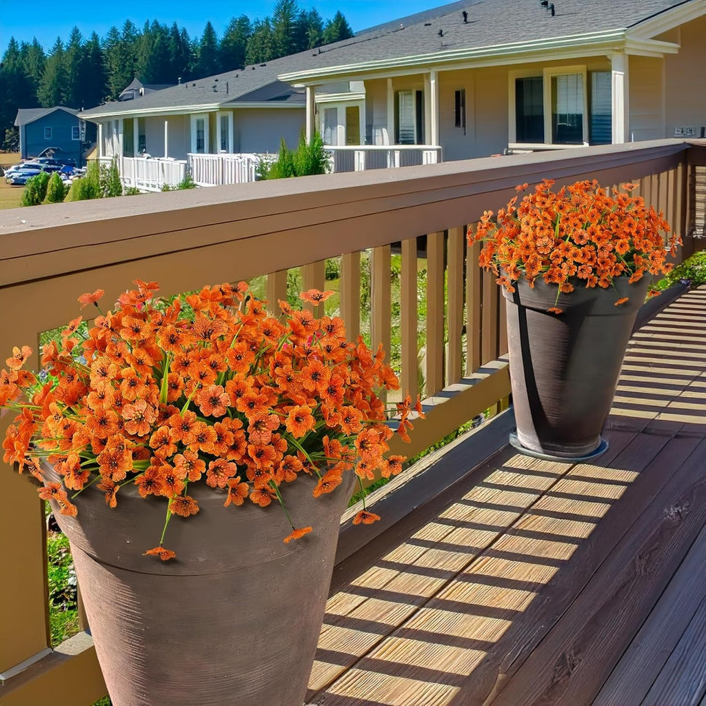 Two potted orange flowers on a wooden deck with a house in the background.