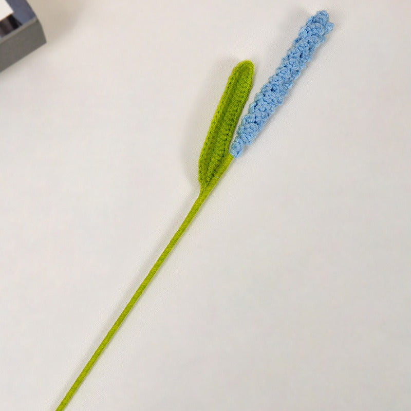 Crocheted flower with green stem and blue bloom on a white background