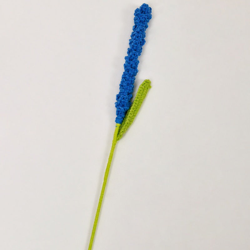 Blue crocheted flower on a green stem against a light gray background