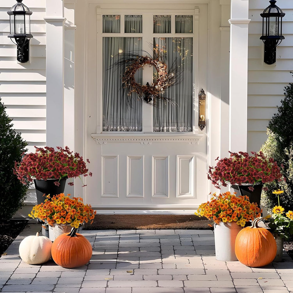Front door with wreath, pumpkins, and flowers on a white house exterior