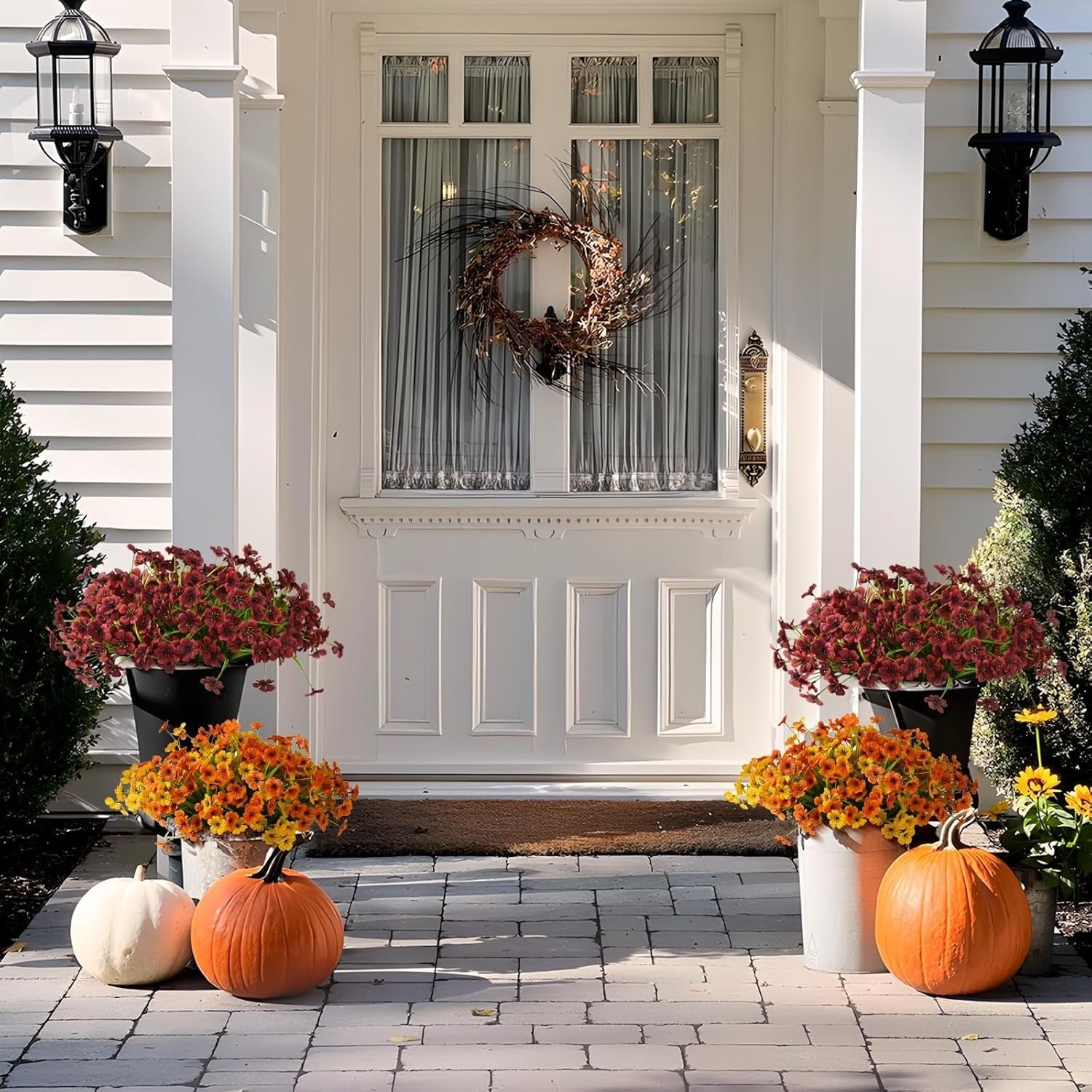 Front door with wreath, pumpkins, and flowers on a white house exterior