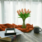 Vase of pink tulips on a table with a mug, book, and framed picture.
