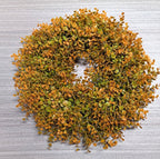 Wreath made of artificial green and orange leaves on a textured gray background