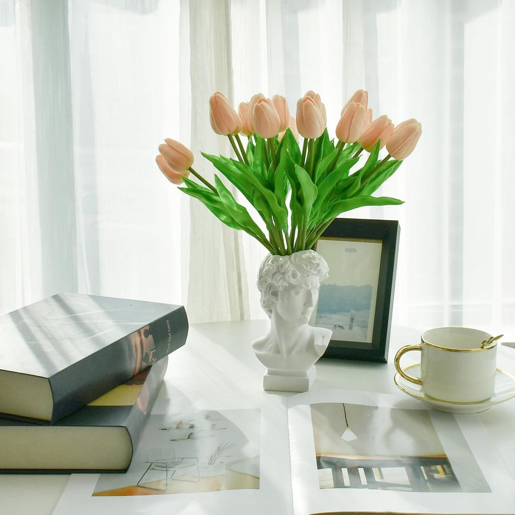 Bouquet of pink tulips in a white vase on a table with books and a cup.