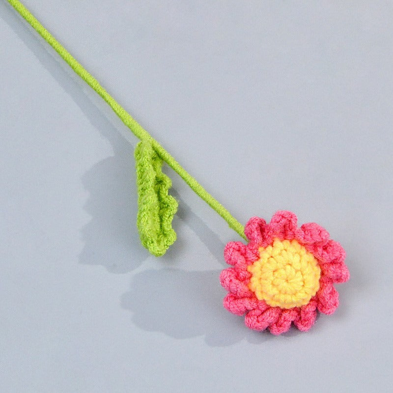 Crocheted flower with pink petals and yellow center on a gray background