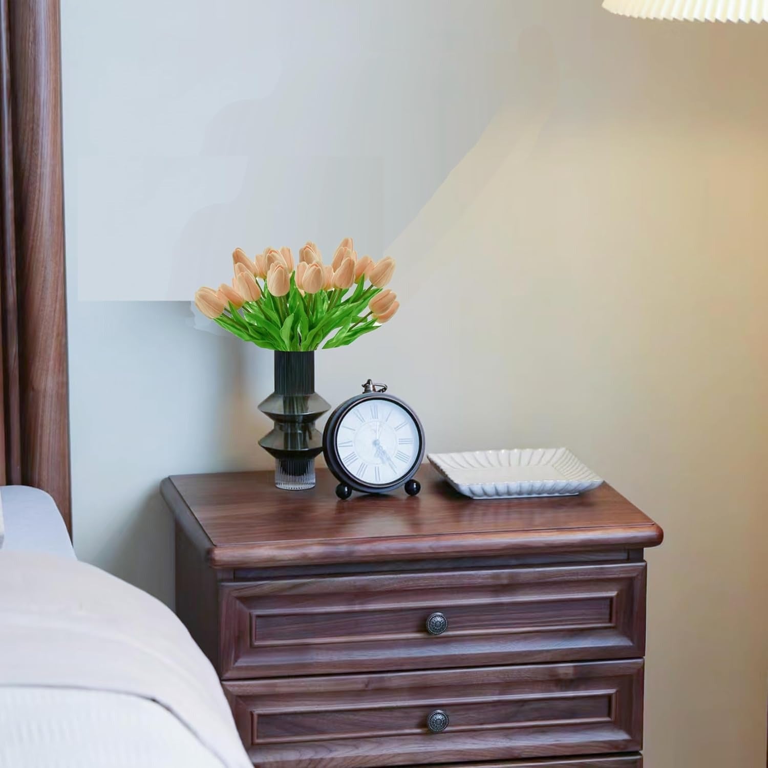 Wooden nightstand with decorative items including a vase of tulips, clock, and square plate.