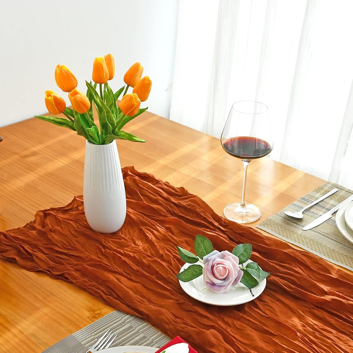 Dining table with orange table runner, vase of tulips, and glass of red wine.