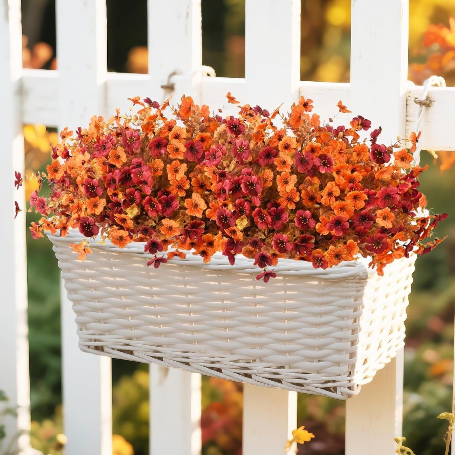 White wicker hanging basket with autumn-colored flowers on a white picket fence.