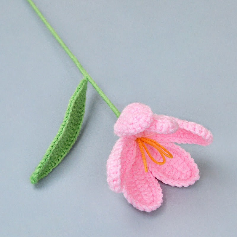 Crocheted pink flower with green stem on a gray background