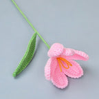 Crocheted pink flower with green stem on a gray background