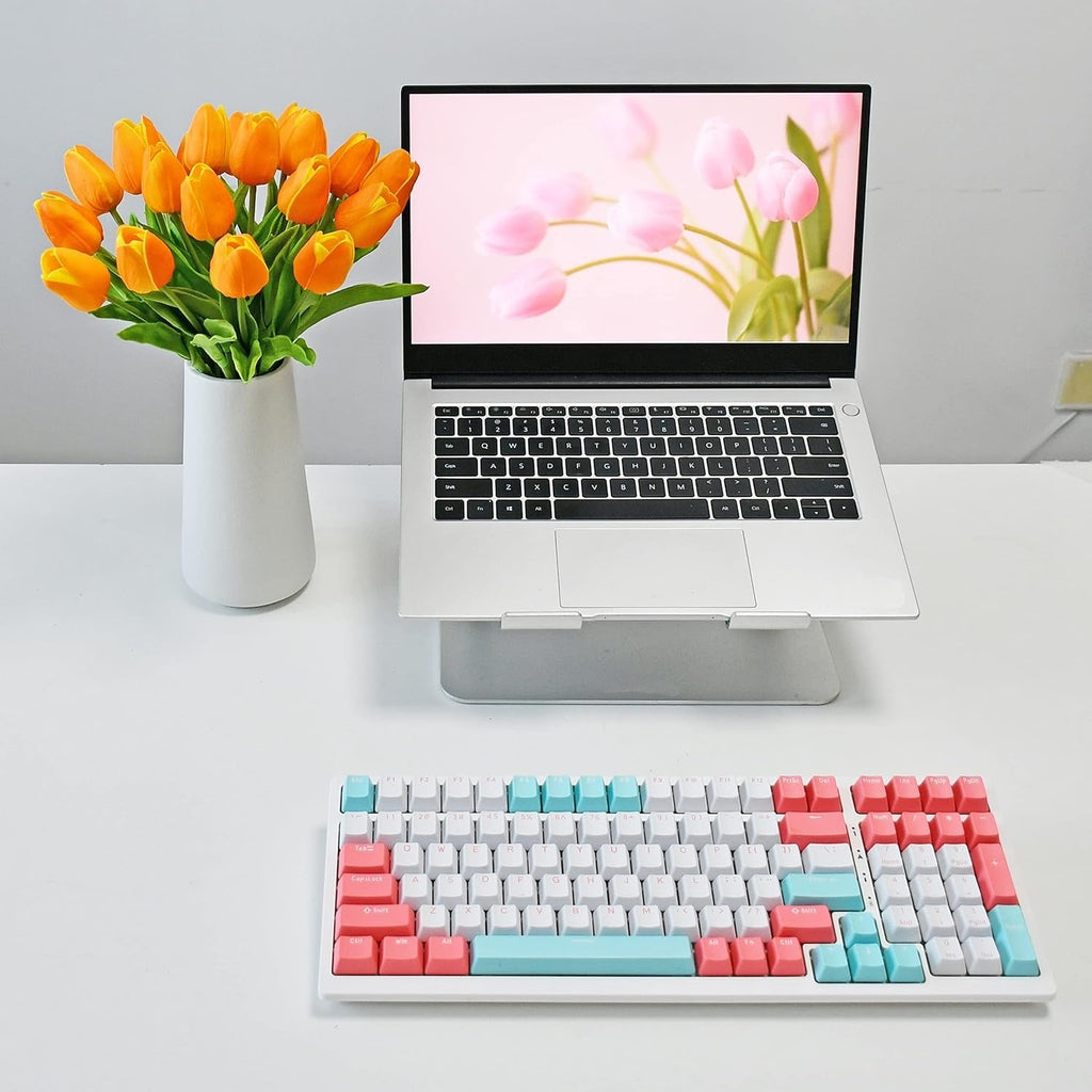 Laptop on a stand with a colorful keyboard and a vase of tulips on a white surface.
