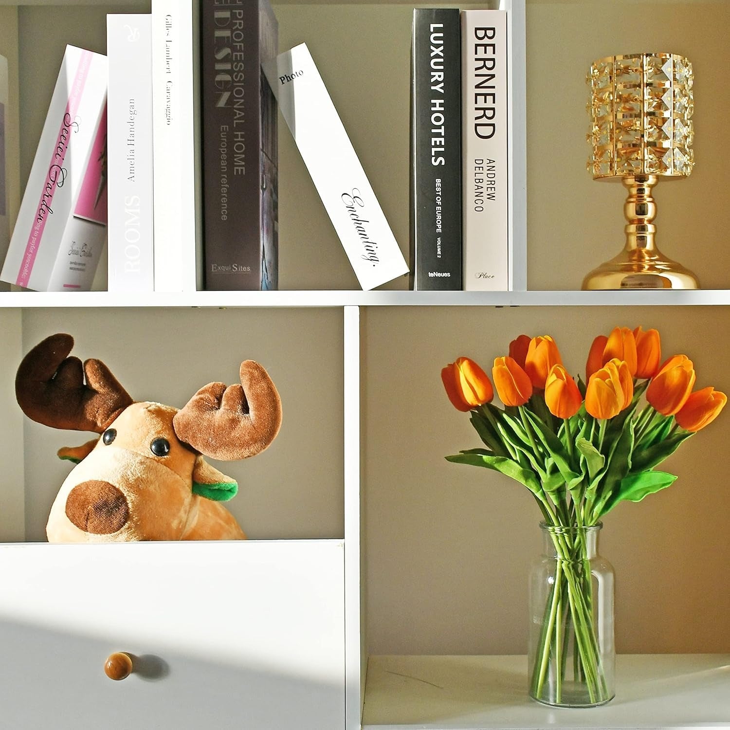Collage of a plush moose, books, a gold lamp, and a vase with orange tulips on a shelf.