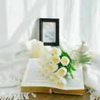 Open book with white tulips, a candle, and a cup on a white blanket