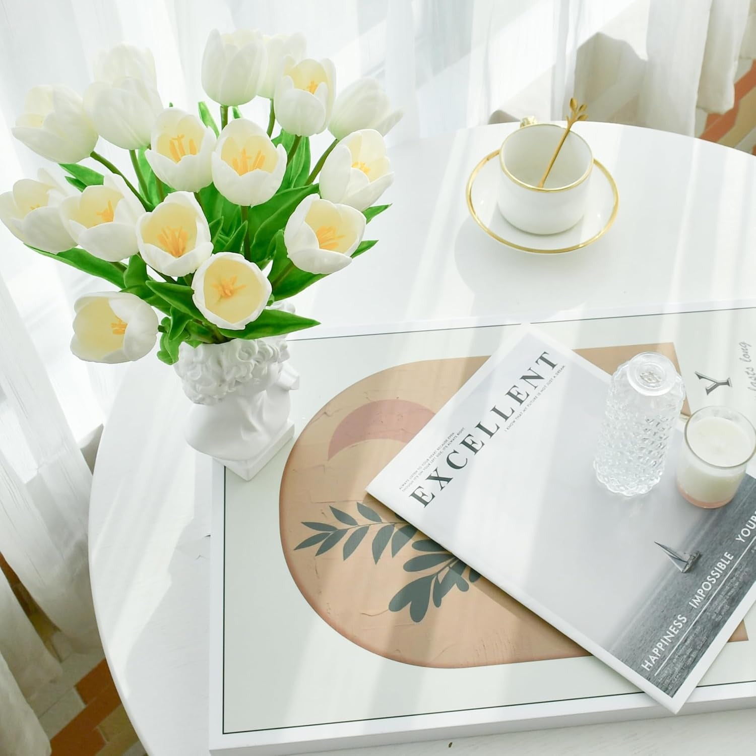 White coffee table with a vase of white tulips, a magazine, and a candle.