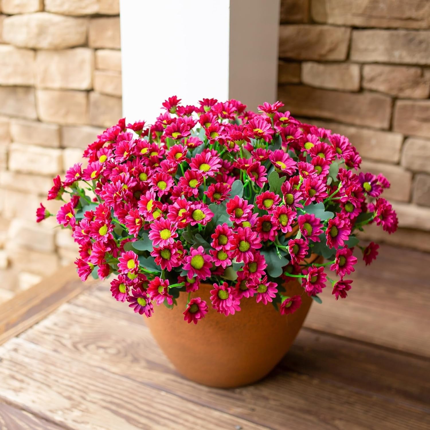 Potted plant with pink flowers on a wooden surface against a stone wall.