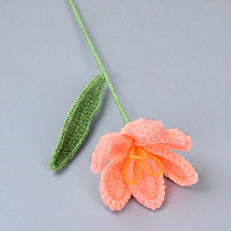 Crocheted pink flower with green leaf on a gray background