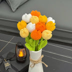 Crocheted flowers in a vase on a dark surface with a lantern and card.