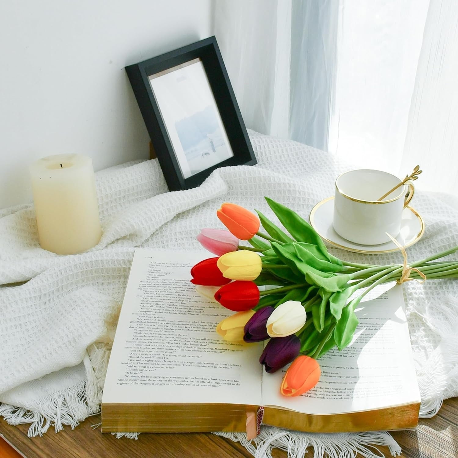Open book with colorful tulips, a cup, and a candle on a white blanket.