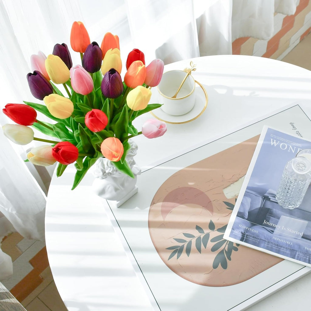 Colorful tulips in a vase on a white table with a magazine and cup.