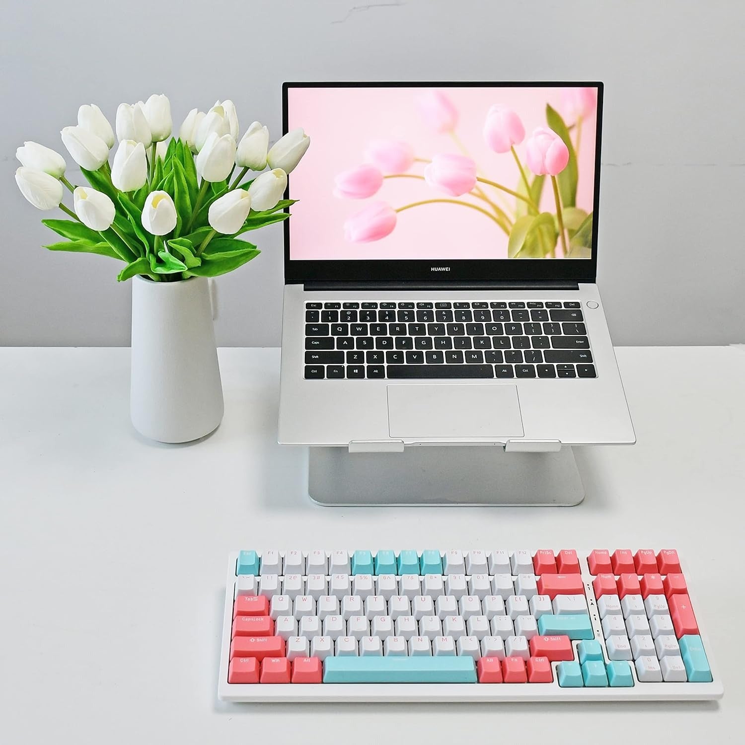 Laptop on a desk with a colorful keyboard and tulips in the background