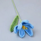 Crocheted blue flower with a green stem on a gray background