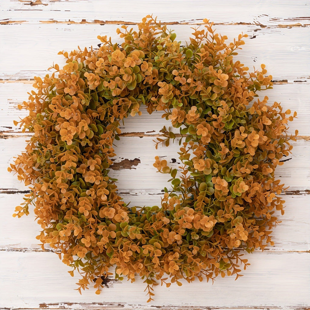 Wreath with orange and green leaves on a white wooden background